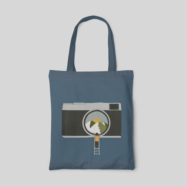 a minimalist designed dark blue tote bag with a boy climbing ladder to a camera's eye which focusing sunrise from the mountain, front side