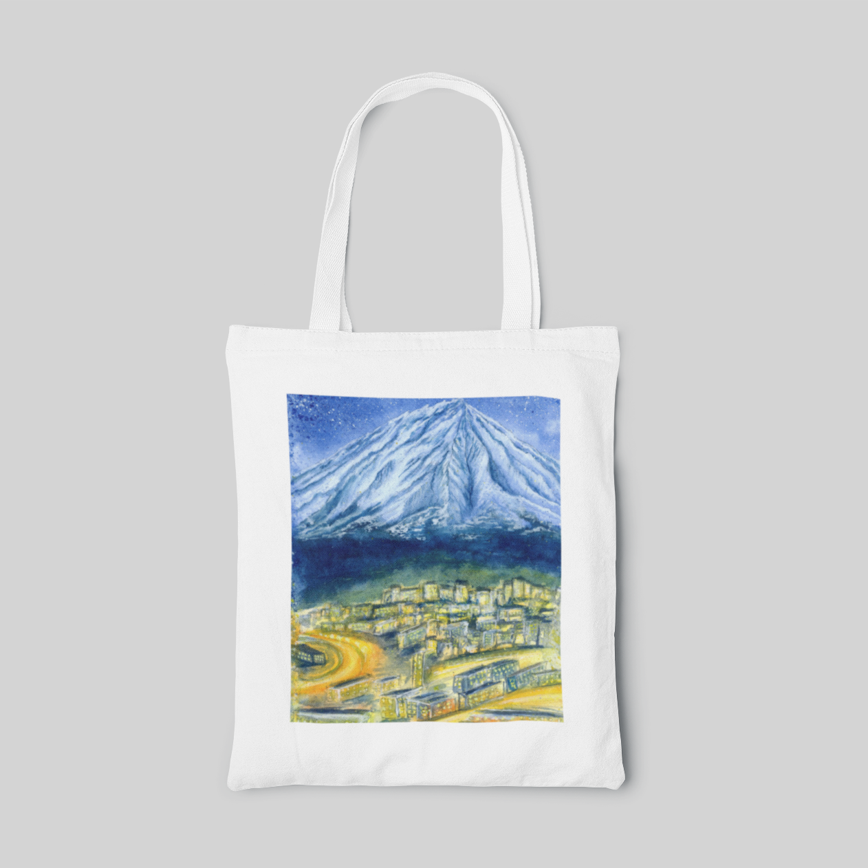 White nature designed tote bag with blue volcano landscape above yellow village, front side
